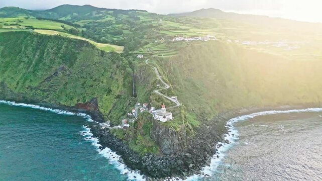 Farol do Arnel lighthouse on seaside Azores cliff, wide aerial pull-out