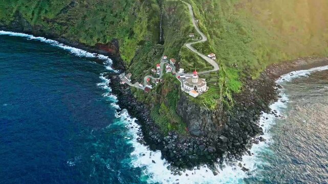 Farol do Arnel lighthouse and green seaside hill in the Azores, wide aerial pan