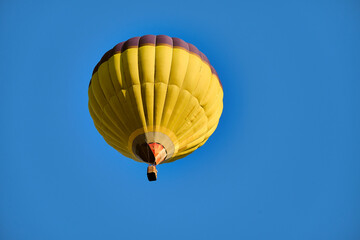 Naklejka premium A vibrant yellow hot air balloon floats gracefully in a clear blue sky, offering a sense of adventure and freedom.