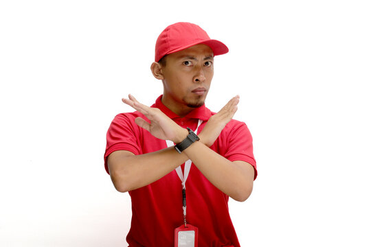 Asian delivery man or courier crosses his arms in a stop or refuse gesture, isolated on white background. Concepts of limitations, restrictions, refusal of service, and boundaries in delivery services