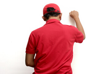 Fototapeta premium Asian delivery man or courier gesturing a knocking-the-door gesture, symbolizing delivering a package to the customer's front door, representing express delivery concept, isolated on white background