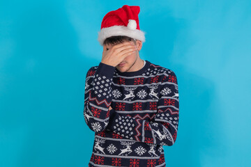 isolated young man with christmas sweater and santa claus hat sad or overwhelmed expression