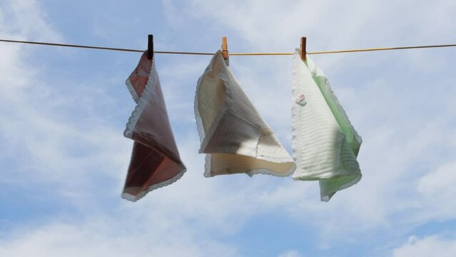 women's panties hang and dry on a clothesline on wooden clothespins and flutter in the wind against the blue sky 4k video