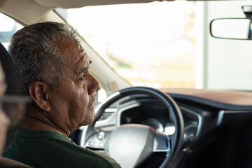 Photograph with copy space of a 60 year old elderly man traveling and driving a modern car, while looking focused on the road with responsibility and freedom to travel during his retirement