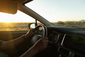 Hands of a man gripping the steering wheel of a car while driving with safety and control, on the road with a panoramic view of the countryside where he is going on a trip