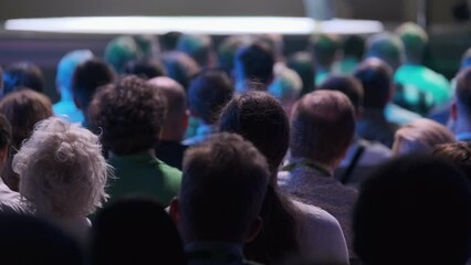 Large audience listening attentively to a speaker at a tech conference. Capturing the focused atmosphere in a dimly lit venue.