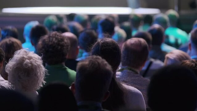 Large audience listening attentively to a speaker at a tech conference. Capturing the focused atmosphere in a dimly lit venue.