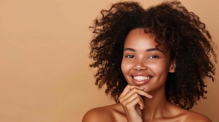 A smiling woman with luscious wavy hair poses with her hand on her chin against a beige backdrop The clear copy space and her radiant complexion make this image ideal for beauty an