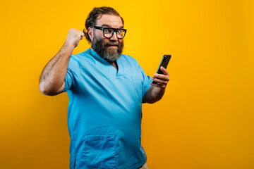 Doctor in blue coat on yellow background using a smartphone.