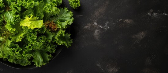 Fototapeta premium Top view of salad leaves mixed in a black bowl on a dark slate, stone, or concrete surface, with ample copy space image.