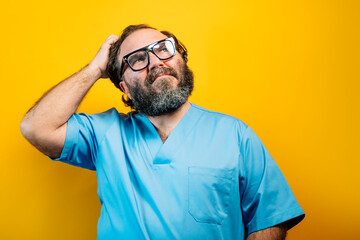 Doctor in blue coat on yellow background gesturing, makes tired gesture with hands on head.