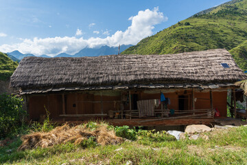 A traditional thatch roof home in the Himalayas. A lone village home with a thatch roof and green and blue scenery.