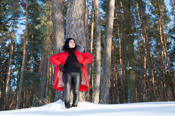 Naklejka premium photo with a young woman in the winter forest. girl in a snowy park. in a red jacket on the banks of a frozen river. winter walk in nature. Cold season. Beautiful girl, sunny day.