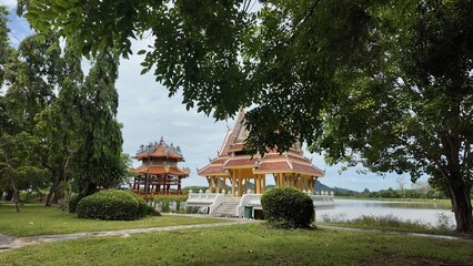 Park with trees, bushes and lawn. A lake, an Asian-style pavilion and hills.