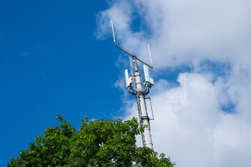 A tall cellular tower stands tall against a blue sky with white clouds. 