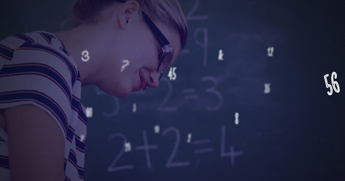 Image of numbers and symbols floating over diverse female teacher teaching a boy at school - Powered by Adobe