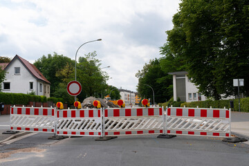 A view of a city street closed for construction work. Red and white barriers block the road.