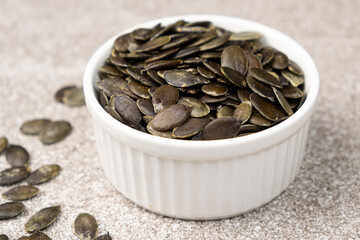 Peeled pumpkin seeds in plate on gray stone background, close-up