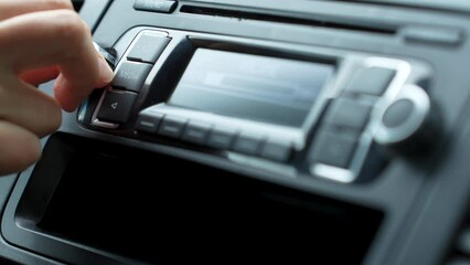 Woman hand turning on car radio, close-up. Driver pressing car radio system