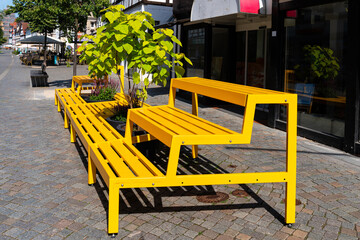 A bright yellow bench with multiple tiers sits on a cobblestone street
