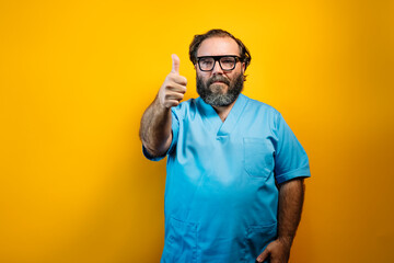 The doctor in a blue coat on a yellow background makes a finger up gesture.