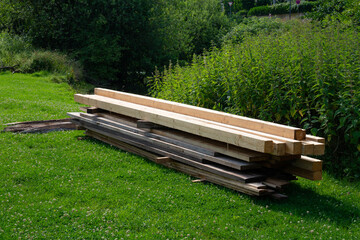 A stack of wooden beams sits on a bed of lush green grass, surrounded by vibrant greenery.