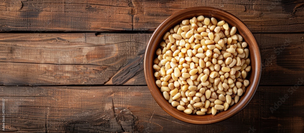 Poster top view of a bowl with pine nuts on a wooden background, providing space for a text overlay or othe