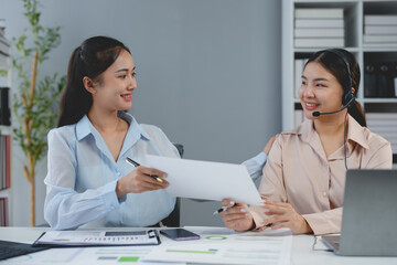 Fototapeta premium Two Asian businesswomen work together using laptops and documents to discuss planning analysis startup project. Customer contact and statistics, online markets, finance and investments at the office.