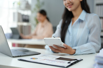 Asian businesswoman works on laptop and calculates with financial calculator from graphs, statistics, charts. Planning. Business success results in modern office.