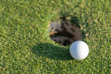 Close-up of golf ball on grass golf course and sunrise background.