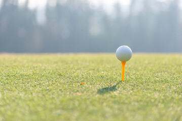 Close-up of golf ball on grass golf course and sunrise background.