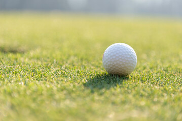 Close-up of golf ball on grass golf course and sunrise background.
