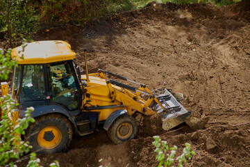 Bulldozer leveling winter soil among green trees, preparation of construction site by bulldozer, soil leveling by bulldozer