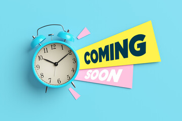 Blue alarm clock is ticking and showing coming soon sign on blue background