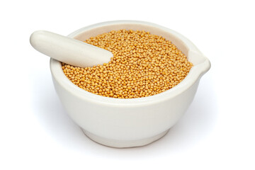 Close-up of Dry Organic Yellow Mustard seeds (Sinapis alba), in white ceramic mortar and pestle, isolated on a white background.