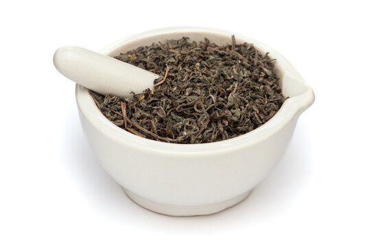 Close-up of Dry Organic Bhringraj (Eclipta prostrata) leaves, in white ceramic mortar and pestle, isolated on a white background.