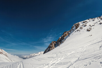 Majestic Winter Landscape: Stunning Views of Central Asian Mountains Above the Clouds with Ski and Snowboard Tracks in Kazakhstan's Almaty Region.