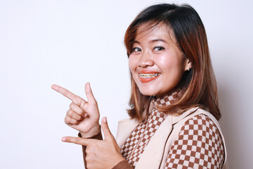 Friendly Asian Mature Woman With Braces Pointing To Side While Looking At Camera Isolated On White Background