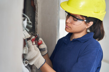 Young female electrician using pliers while fixing cables at incomplete house construction site