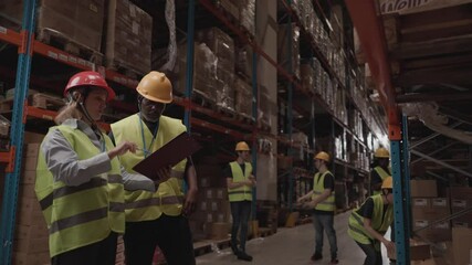 Team of multiracial warehouse workers, wearing security gear discussing inventory while checking clipboard. Busy warehouse environment. Warehouse workers discussing inventory - Powered by Adobe