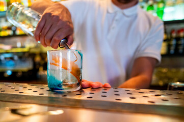 A bartender skillfully pours a vibrant cocktail into a glass, showcasing the art of mixology