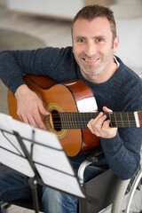 Obraz premium smiling man in a wheelchair practicing the guitar