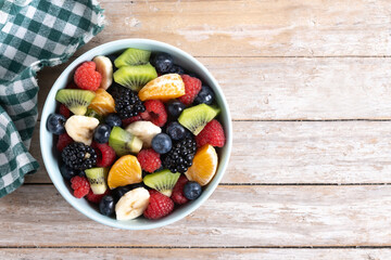 Fruit salad in a blue bowl on wooden table. Top view. Copy space