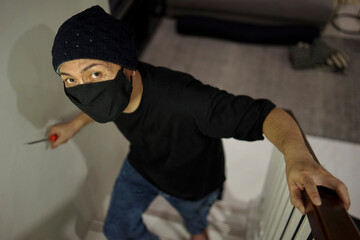 Top View Of Burglar Man Wearing A Mask Walking On Stairs With A Screw Driver For The Loot