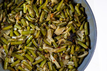 Spicy green beans curry with white onion, in frying pan, cooked indian style, vegetarian dish, top view on white background.