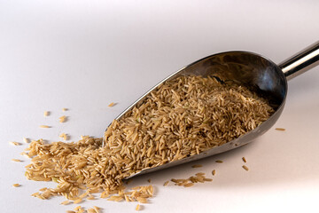 Raw Basmati brown rice spilling out of a metal scoop on white background