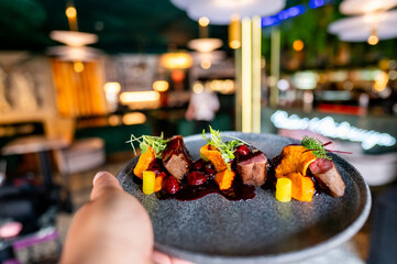 Close-up of a hand presenting a vibrant, artistically plated gourmet dish