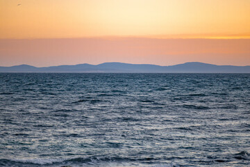 Beautiful sunset over sea with reflection in water and hills in background