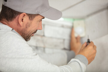 Fototapeta premium male electrician installing detector on wall