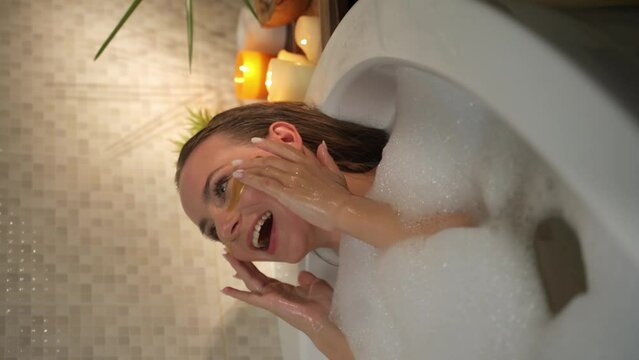 Vertical Screen: A woman relaxes in a bubble bath, wearing eye patches. She is surrounded by bubbles and candles. The atmosphere is calm and relaxing